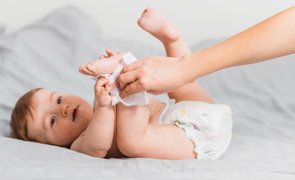 Imagem de uma mãe limpando o pé de um bebê com fralda trocada, simbolizando a importância do kit higiene.