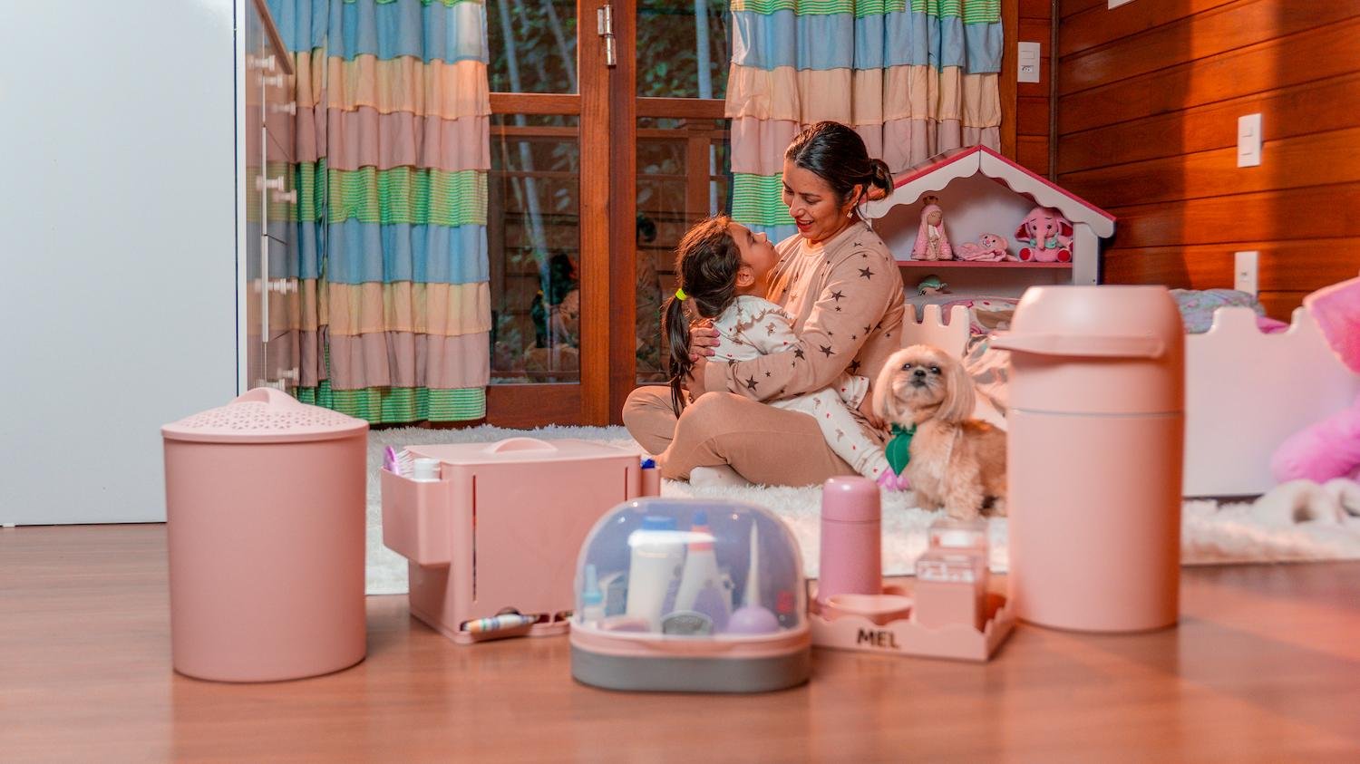 M&atilde;e e filha no quarto com produtos BabyMel, incluindo cesto de roupa, organizador de fraldas, frasqueira e kit higiene personalizado