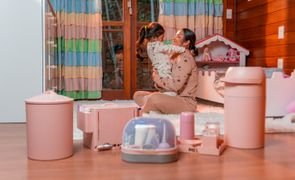 Mãe e filha no quarto com produtos de higiene do bebê como lixeira, cesto, frasqueira e potes