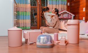 Mãe e filha no quarto com produtos de higiene do bebê como lixeira, cesto, frasqueira e potes