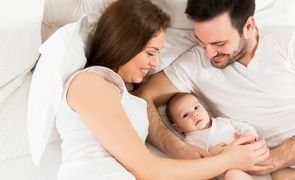 Família com recém-nascido na cama, ilustrando como cuidar de bebê com carinho e segurança no dia a dia