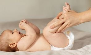 Bebê deitado em trocador enquanto um adulto limpa e troca a fralda, ilustrando o descarte de fraldas