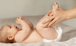 Bebê deitado em trocador enquanto um adulto limpa e troca a fralda, ilustrando o descarte de fraldas