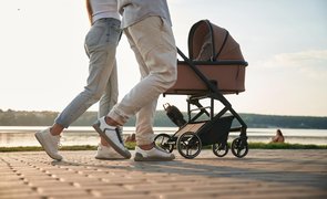 Pais caminhando ao ar livre empurrando um carrinho de bebê em um parque à beira de um lago